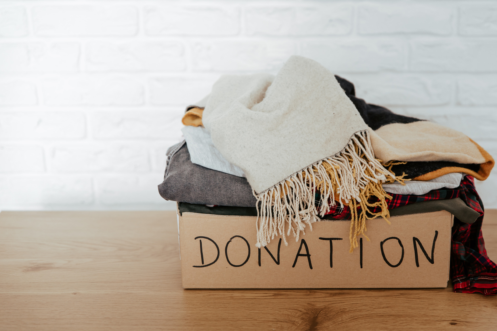 Cardboard donation box on the table full with used clothes.